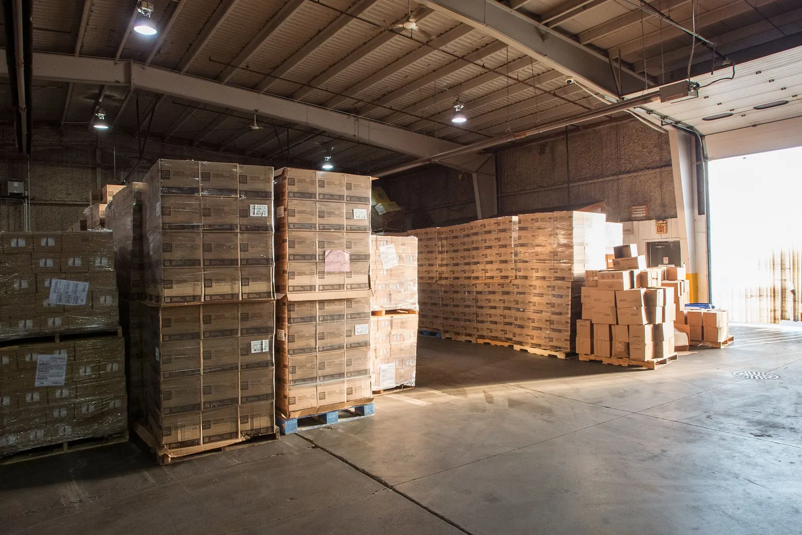 Muelle de carga con palés de cajas retractiladas junto a una puerta seccional abierta